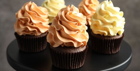 Delicious cupcakes with colorful cream against black stand on grey background, closeup