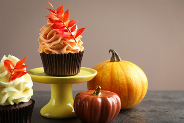 Delicious cupcakes with branches with red leaves and decorative pumpkins on grey textured table, closeup. Autumn atmosphere