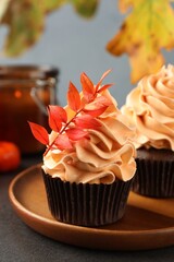 Delicious cupcakes with branch with red leaves on grey textured table, closeup. Autumn atmosphere