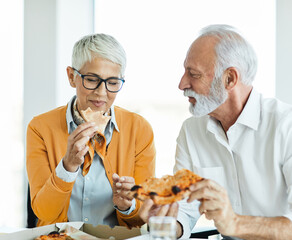 Portrait of two senior businesspeople, elderly business woman and man having a meeting or a break eating pizza in the office.
