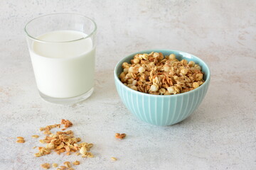 Granola cereal in a blue bowl with milk in a glass for breakfast on a white surface