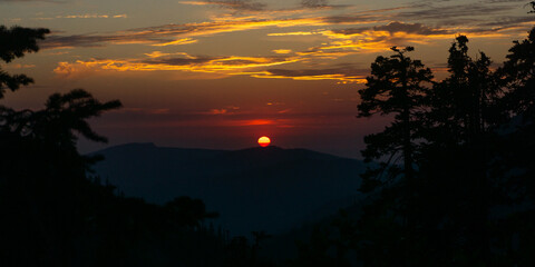 A scenic view of a sunset with a vibrant orange sky over the mountains and silhouetted trees