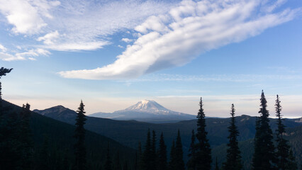 Mountain view with pine trees in foreground and clouds in the sky on a bright sunny day