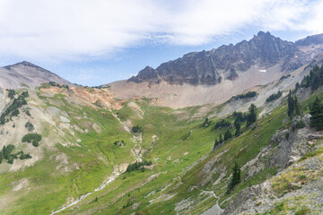 Obraz premium Aerial view of mountain range with green slopes and rocky peaks under a cloudy blue sky landscape scene