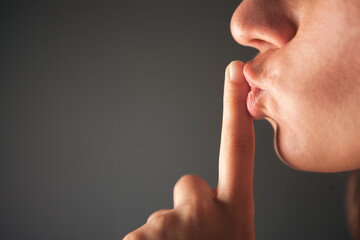Close up of a woman's lips making silence gesture on grey background