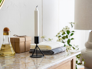 White candle on black stand with stacked towels and oil bottle