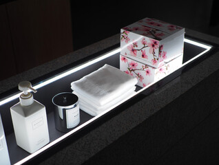 White soap dispenser silver candle and stacked white towels with floral boxes