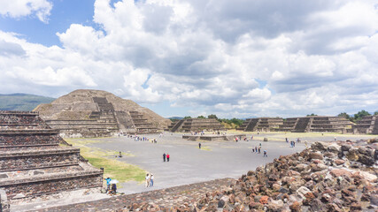 Tourists exploring the ancient ruins of Teotihuac&aacute;n in Mexico. The image highlights the vast archaeological site and its famous pyramids under a bright blue sky.