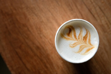 Top view of a beautifully crafted latte art in a ceramic cup, featuring intricate leaf design, resting on a dark surface, showcasing the artistry of coffee preparation and presentation