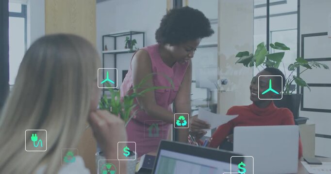 Two women reviewing paper, colleague taking it, starting floating energy icons for green project