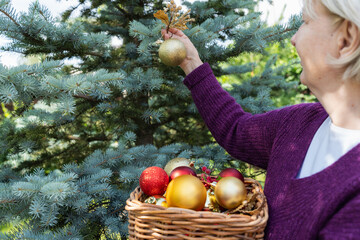 caucasian woman decorating an outdoor Christmas tree with a golden ornament and festive baubles.