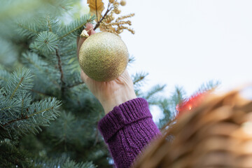 Hand decorating an outdoor Christmas tree with a golden ornament and festive baubles.