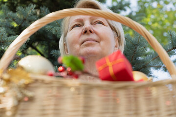 Elderly caucasian woman holding a basket with holiday ornaments outdoors, festive mood concept.