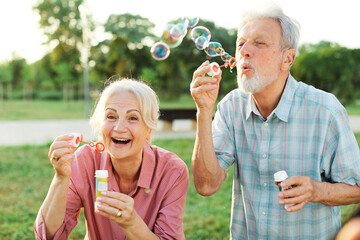 Happy active senior couple having fun blowing soap bubbles in park outdoors. Vitality and active senior couple concept