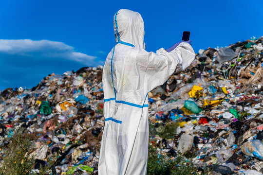 Individual wearing a protective suit captures a moment at a large garbage dump, surrounded by heaps of waste under a clear sky
