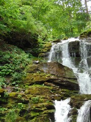 A beautiful natural waterfall cascades over mossy rocks in a lush green forest, creating a peaceful and refreshing atmosphere surrounded by vibrant foliage and flowing water