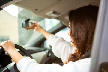 Young woman adjusting rearview mirror while driving car