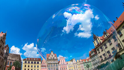 Transparent soap bubble reflects the historic, colorful facades of Old Town Market Square in Wroclaw, Poland. This bright, sunny image with a deep blue sky evokes feelings of joy, summer, and magic.