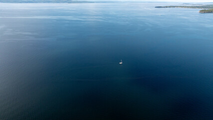 A lone sailboat drifts across the calm, expansive blue waters of Lake Champlain on a clear day.