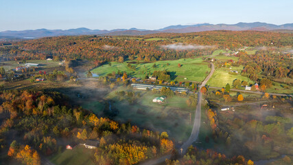 Foggy autumn sunrise over colorful farmland, trees, and rolling hills in Stowe, Vermont.