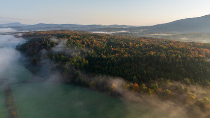 Foggy autumn sunrise over colorful farmland, trees, and rolling hills in Stowe, Vermont.