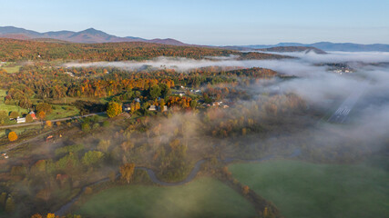 Foggy autumn sunrise over colorful farmland, trees, and rolling hills in Stowe, Vermont.