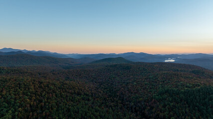 Rolling forested hills of the Adirondack Mountains at sunrise, bathed in soft light with autumn colors emerging.