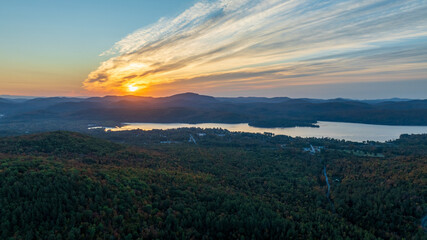Sunrise over Schroon Lake with colorful skies reflecting on water and surrounding forested Adirondack mountains.