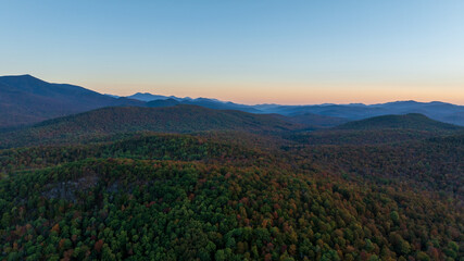 Rolling forested hills of the Adirondack Mountains at sunrise, bathed in soft light with autumn...