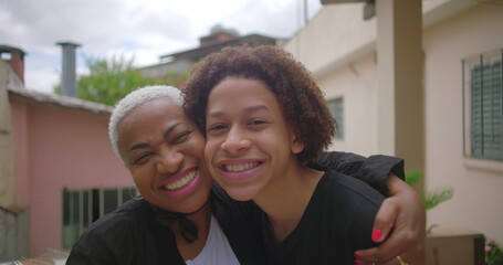 Obraz premium Latino teenage boy from African descent kissing his mother’s cheek, both smiling warmly, expressing deep love and affection in a joyful family moment on a Latin American terrace