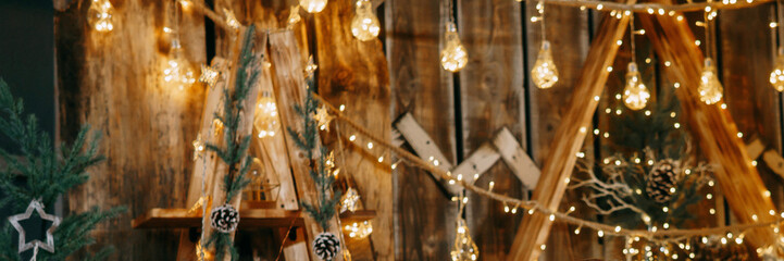 Decorated Christmas interior with glowing light bulbs and garland with evergreen pine branches and cones. Holiday decoration and festive mood.