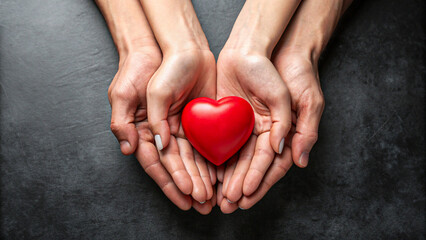 Hands holding red heart symbol on dark background
