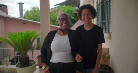 Latin woman of African descent smiling warmly with her teenage son, standing together on a sunny...