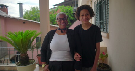 Latin woman of African descent smiling warmly with her teenage son, standing together on a sunny...