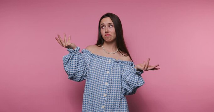 footage of young woman expresses confusion while dressed in a blue gingham outfit on pink background