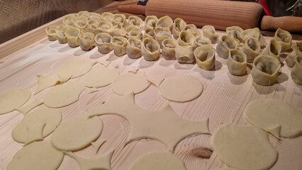 The intricate process of making fresh pasta from scratch, with cut dough circles and scraps in foreground and rows of finished tortellini on wooden board, ready for cooking in kitchen or restaurant