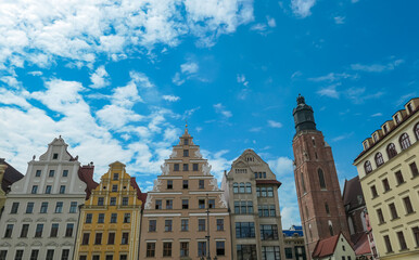 Fototapeta premium Decorative gabled buildings and a tall brick church tower rise beneath scattered clouds, showcasing Wroclaw’s Old Town charm and the architectural diversity of this Polish cultural hub.