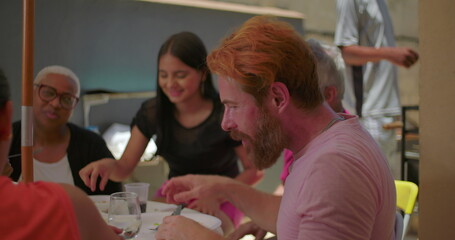 Bearded man drinking water at a backyard BBQ lunch with family and friends, seated at an outdoor...