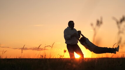Silhouette father tossing and spinning child, sunset sky and sun, parent with daughter outdoors,...