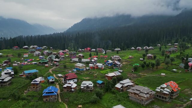 Aerial View of Arang Kel, Azad Kashmir &mdash; Scenic Mountain Village with Colorful Houses, Lush Greenery, and Misty Hills Surrounded by Dense Pine Forests on a Cloudy Day