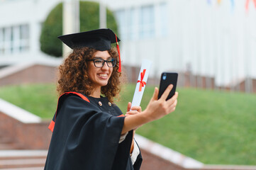 Female student graduate celebrating diploma with smartphone selfie
