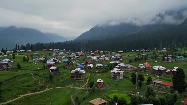 Aerial View of Arang Kel, Azad Kashmir &mdash; Scenic Mountain Village with Colorful Houses, Lush Greenery, and Misty Hills Surrounded by Dense Pine Forests on a Cloudy Day
