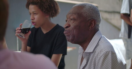 Elderly man interacting with family members during outdoor meal, multigenerational bonding and candid BBQ scene in backyard setting