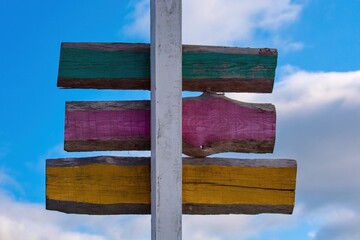 Colorful wooden signpost with blank painted boards in green, pink, and yellow, standing against blue sky with clouds. Ideal for travel, navigation, and direction concepts.
