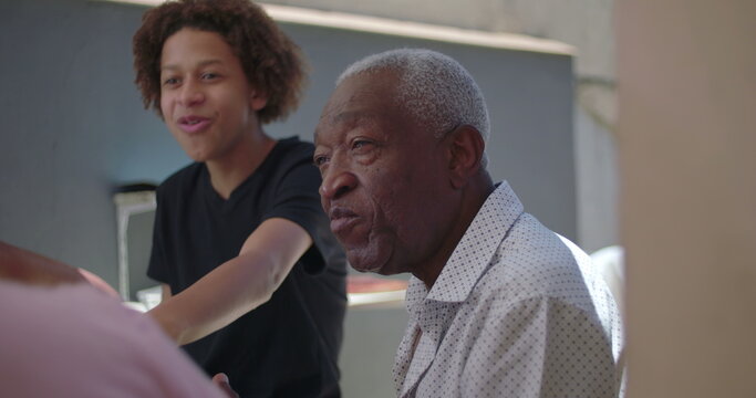 Teenager and grandfather sharing laughter during a family meal outdoors, highlighting generational connection, joy, and warmth in a diverse family setting - Powered by Adobe