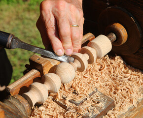 Experienced artisan wearing a simple gold band working wood block using old turning equipment and sharp chisel