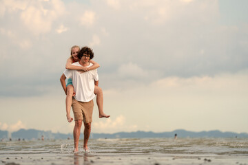 Happy young couple enjoying playful piggyback ride at the beach during sunset. Perfect for concepts like romance, summer vacation, freedom, fun, and relationship lifestyle imagery.