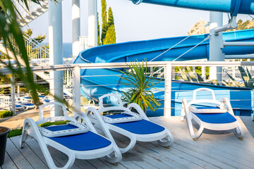 Water Park Lounge Chairs Relaxation - White lounge chairs on a wooden deck overlooking a water park with blue slides.