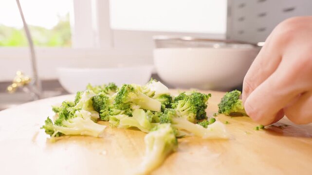 Closeup of Hand Slicing Broccoli on Round Wooden Board with Natural Light from Window, Healthy Cooking Concept