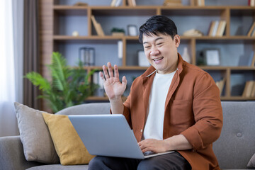 Asian man waving on video call using laptop
